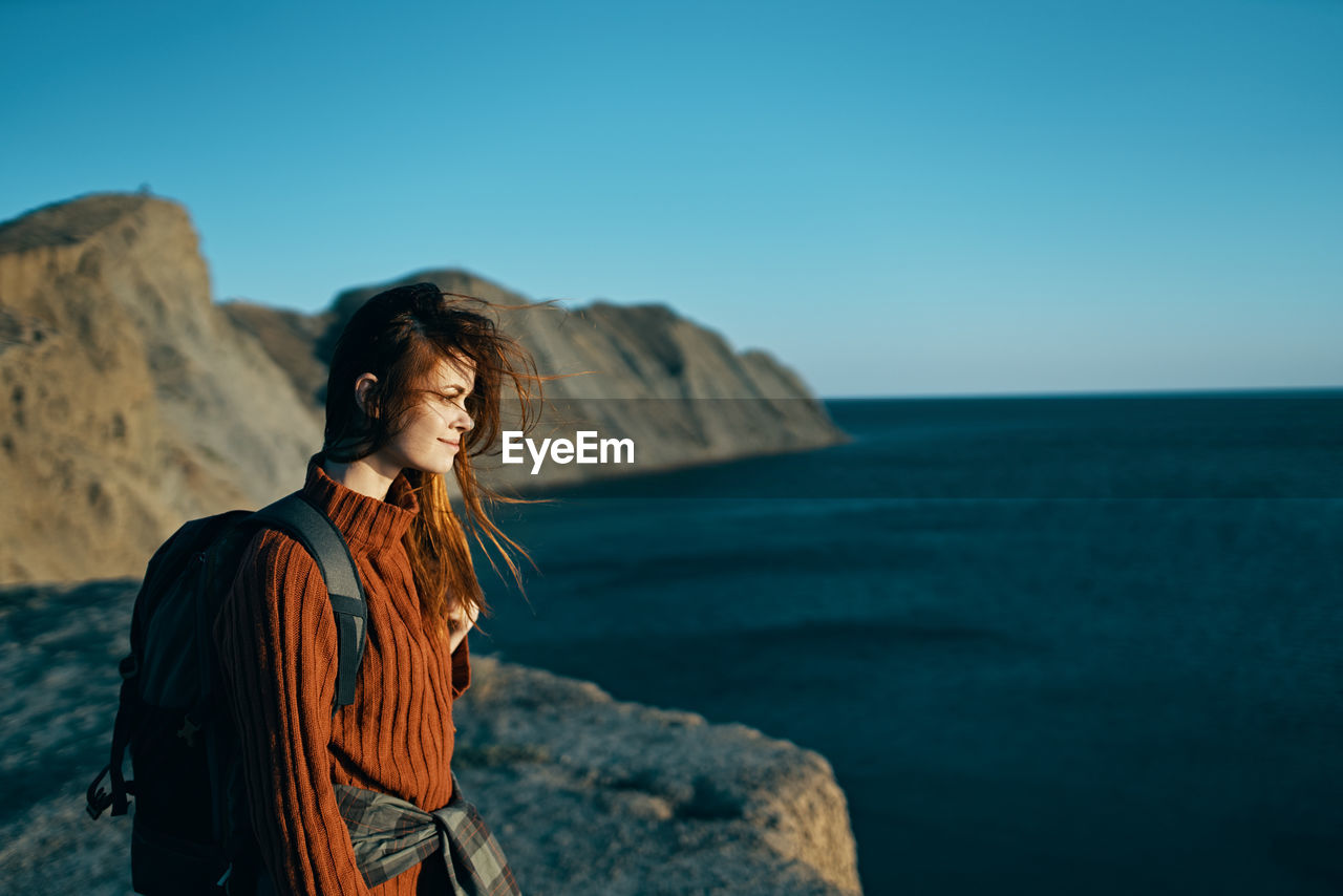 YOUNG WOMAN STANDING ON ROCK AGAINST SEA