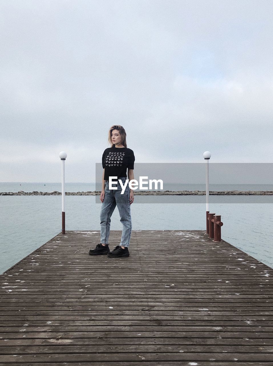 water, sky, full length, one person, pier, sea, cloud, nature, shore, boardwalk, casual clothing, standing, men, walkway, coast, ocean, day, wood, jetty, leisure activity, front view, childhood, child, beach, lifestyles, overcast, beauty in nature, looking at camera, outdoors, portrait, scenics - nature, land, adult, tranquility, architecture, horizon over water, holiday, copy space, footwear, vacation, trip, horizon, clothing