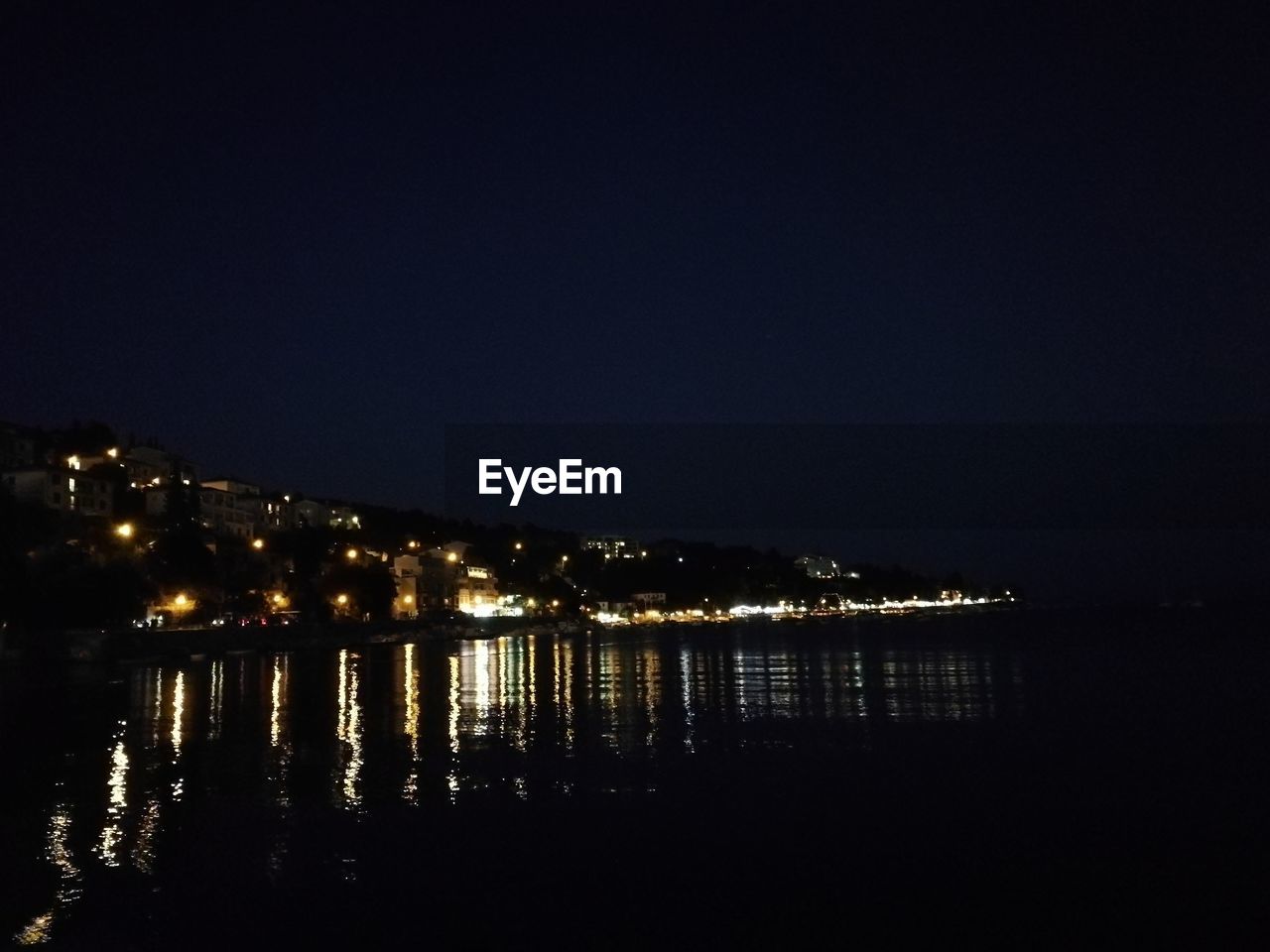 ILLUMINATED CITY BY RIVER AGAINST CLEAR SKY