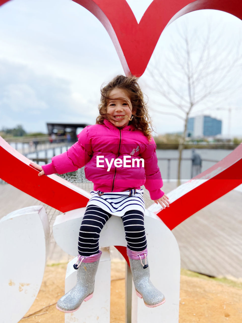 Portrait of smiling young woman standing in city next to heart statue 