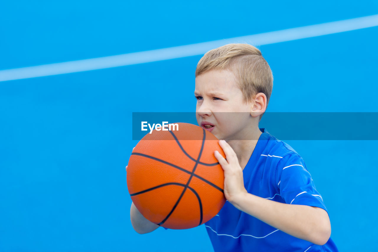 Boy aiming basketball while standing on sports court