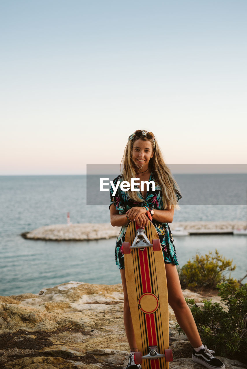 Young female with long board skate in front of the mediterranean sea