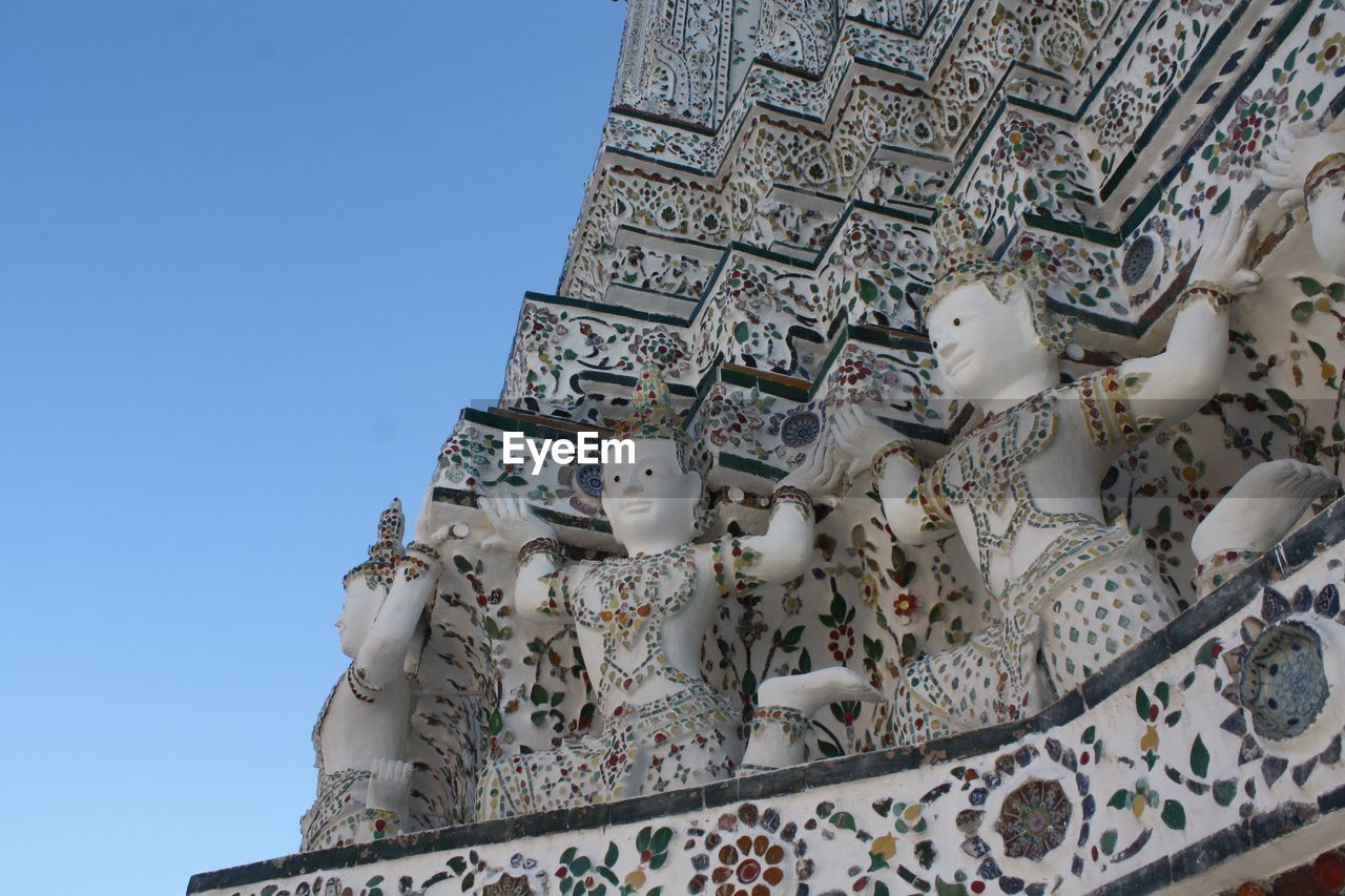 Low angle view of statues at wat arun against clear blue sky