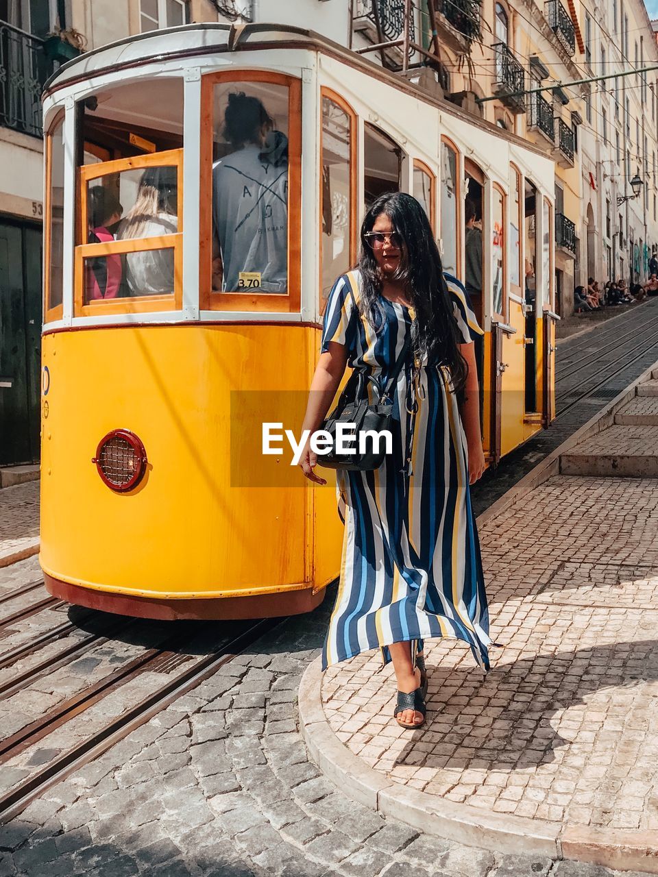 Full length portrait of young woman standing by tram in city