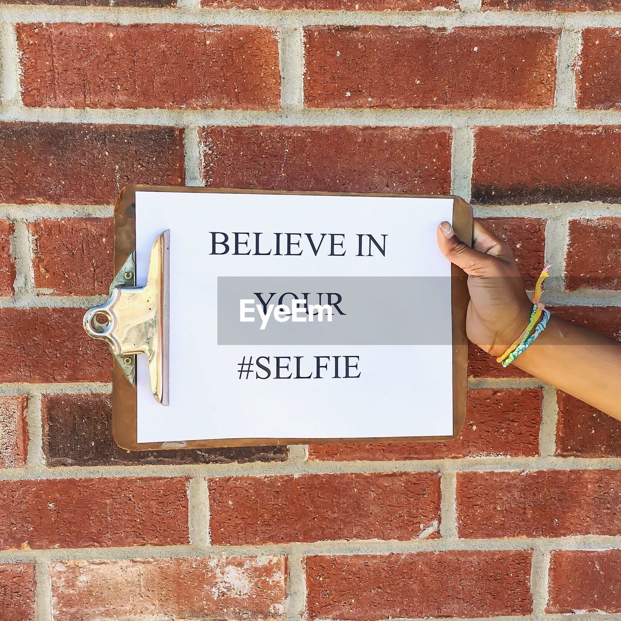 Cropped image of person holding clipboard with text against brick wall