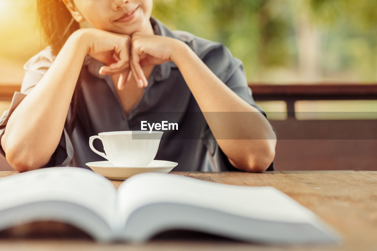 Midsection of woman with coffee cup on table