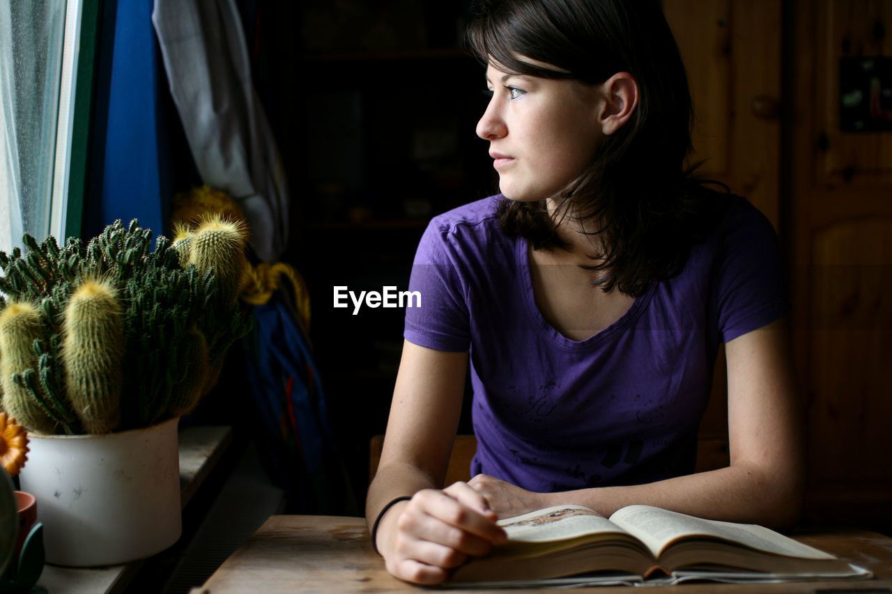 Smiling young woman looking away while sitting on table at home