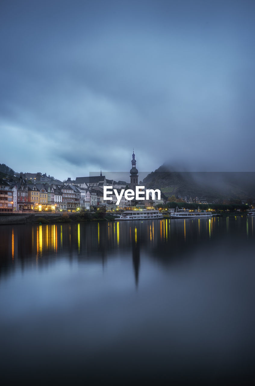 Illuminated bridge over river with city in background