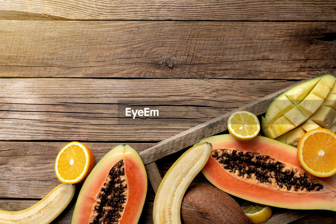 Fresh tropical fruits in a wooden delivery box on wooden background. papaya, orange, banana, coconut