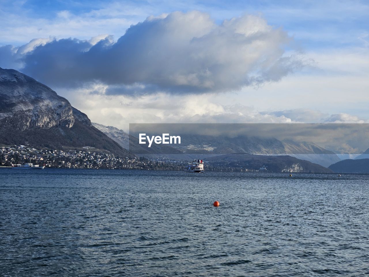 Scenic view of lake and mountains against sky with beautiful white clouds