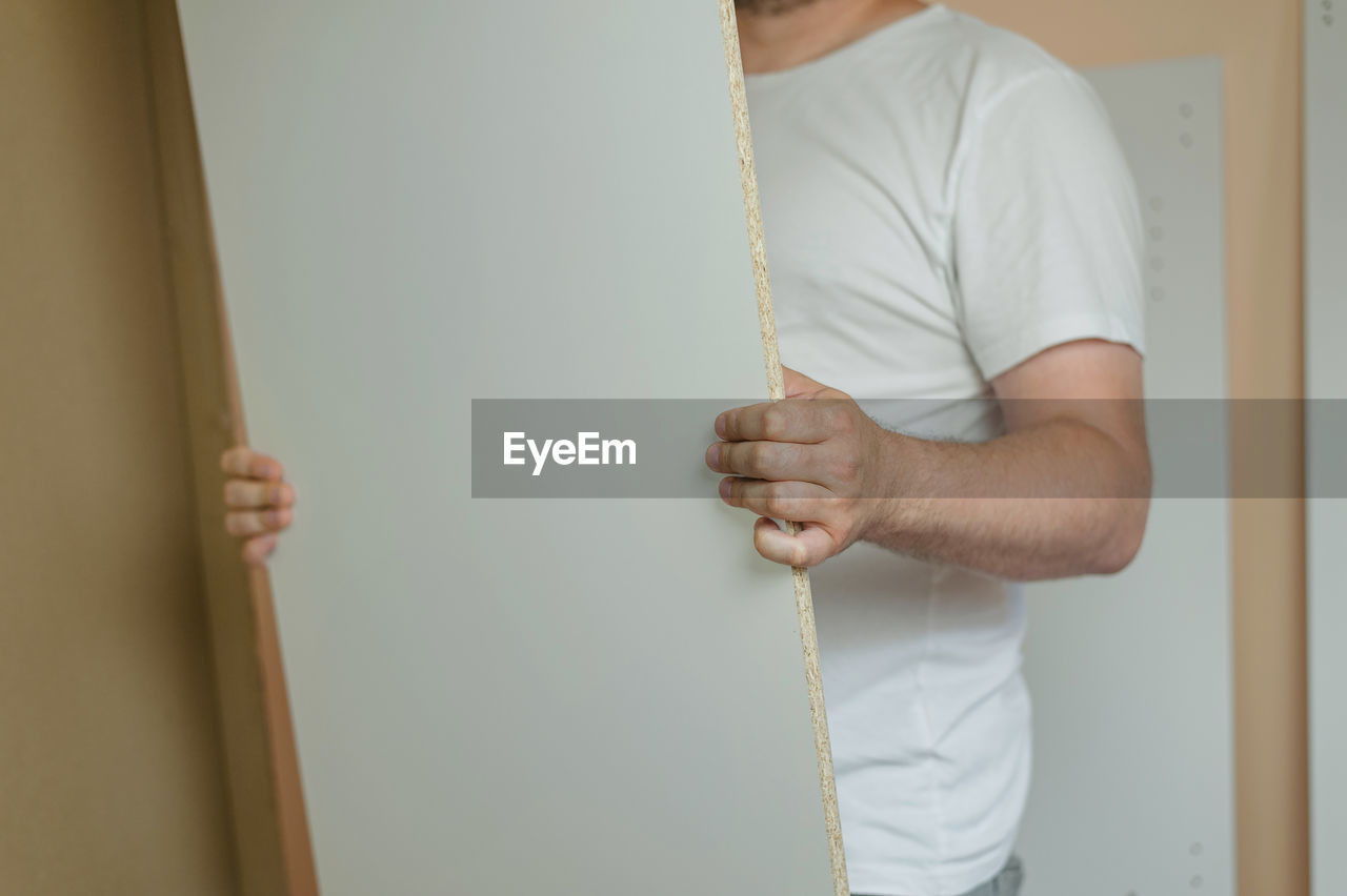 Midsection of man holding plywood at home