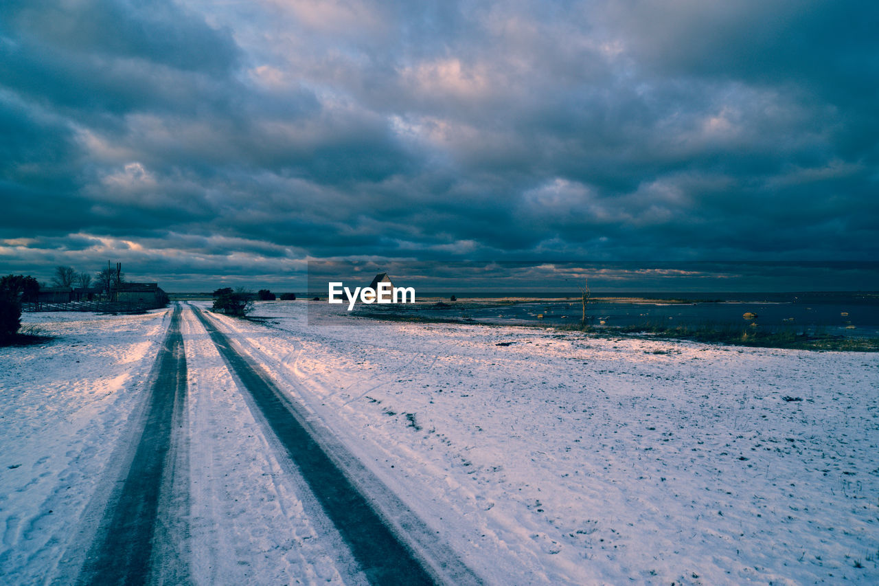 Tire tracks on snow covered road against sky