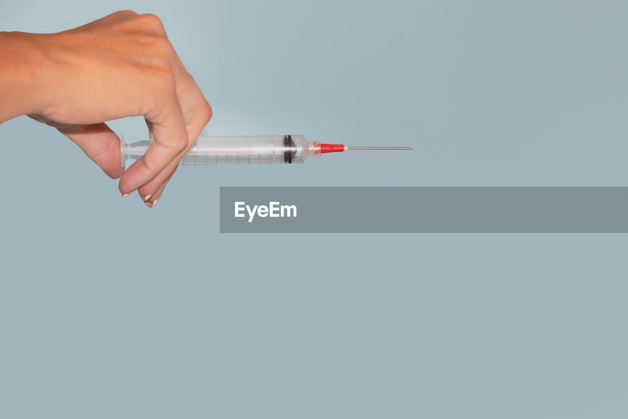 Cropped hand of person holding syringe against gray background