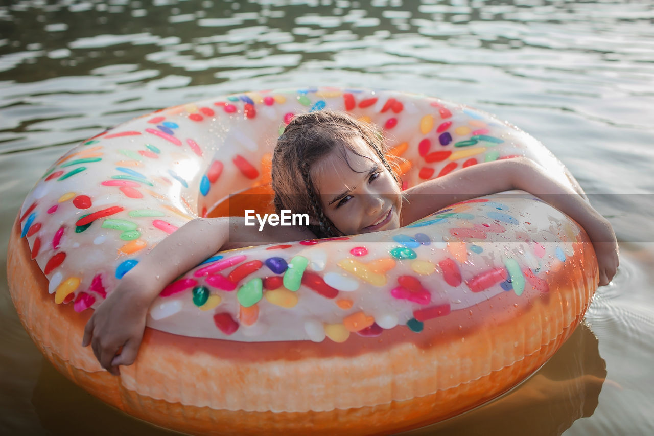 Girl swims with big donut inflatable ring on lake on hot summer day, happy summertime, cottagecore