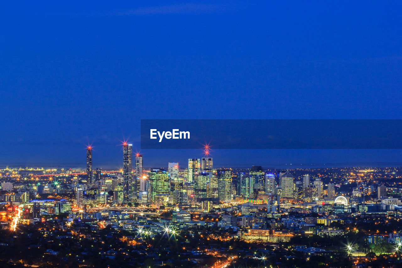 HIGH ANGLE VIEW OF ILLUMINATED BUILDINGS AGAINST BLUE SKY AT NIGHT