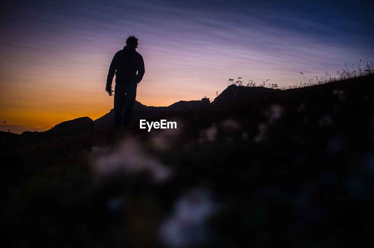 Silhouette man standing on rock against sky during sunset