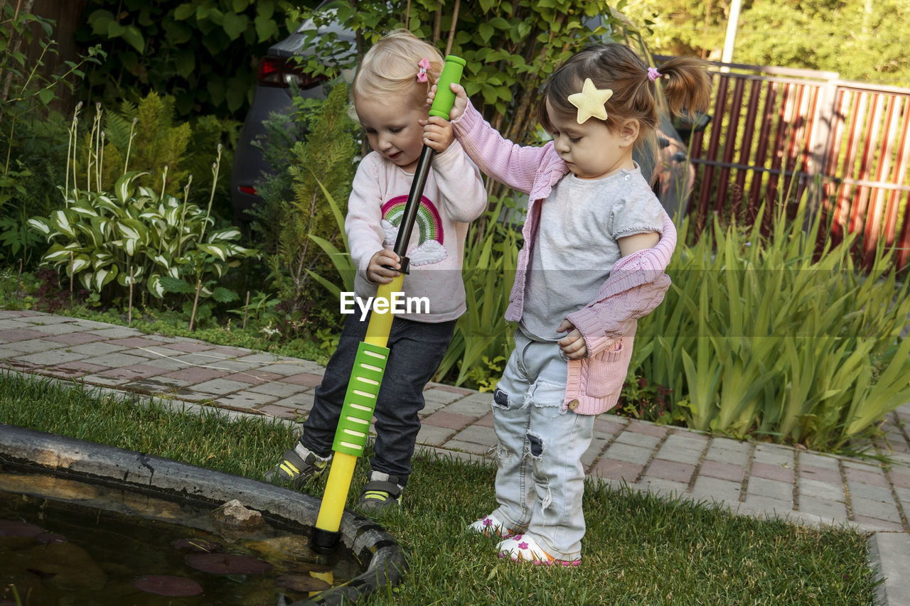 Two girls pumping water with children's pumps from a small pond.
