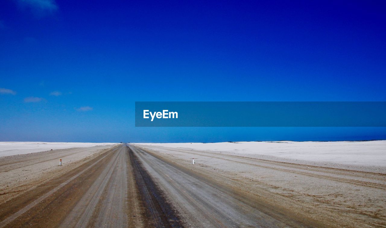 Road amidst land against clear blue sky