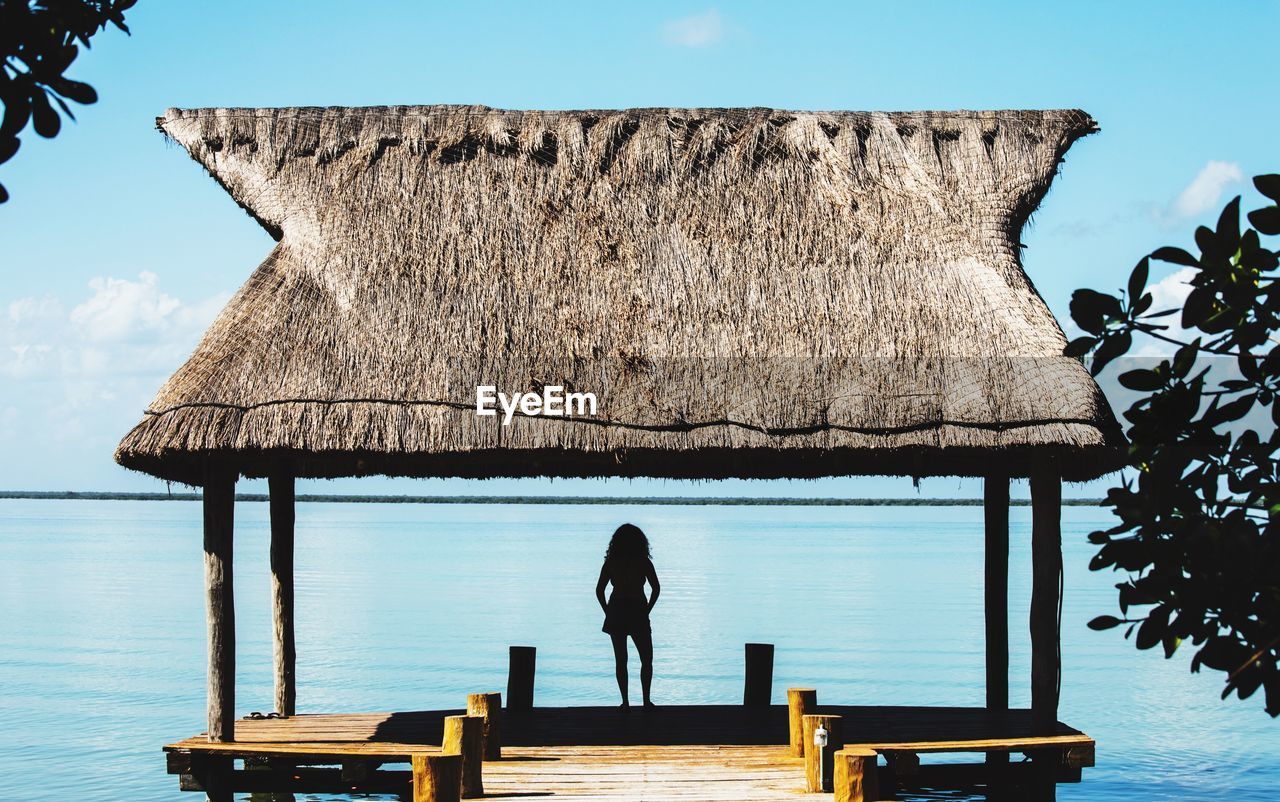 Rear view of silhouette woman standing in gazebo on pier over sea