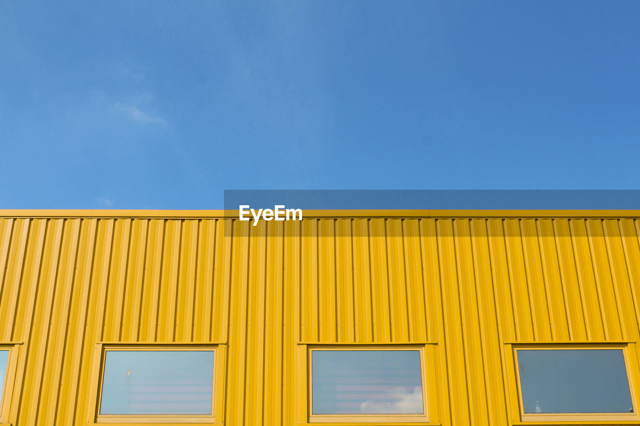 Low angle view of yellow building against clear blue sky