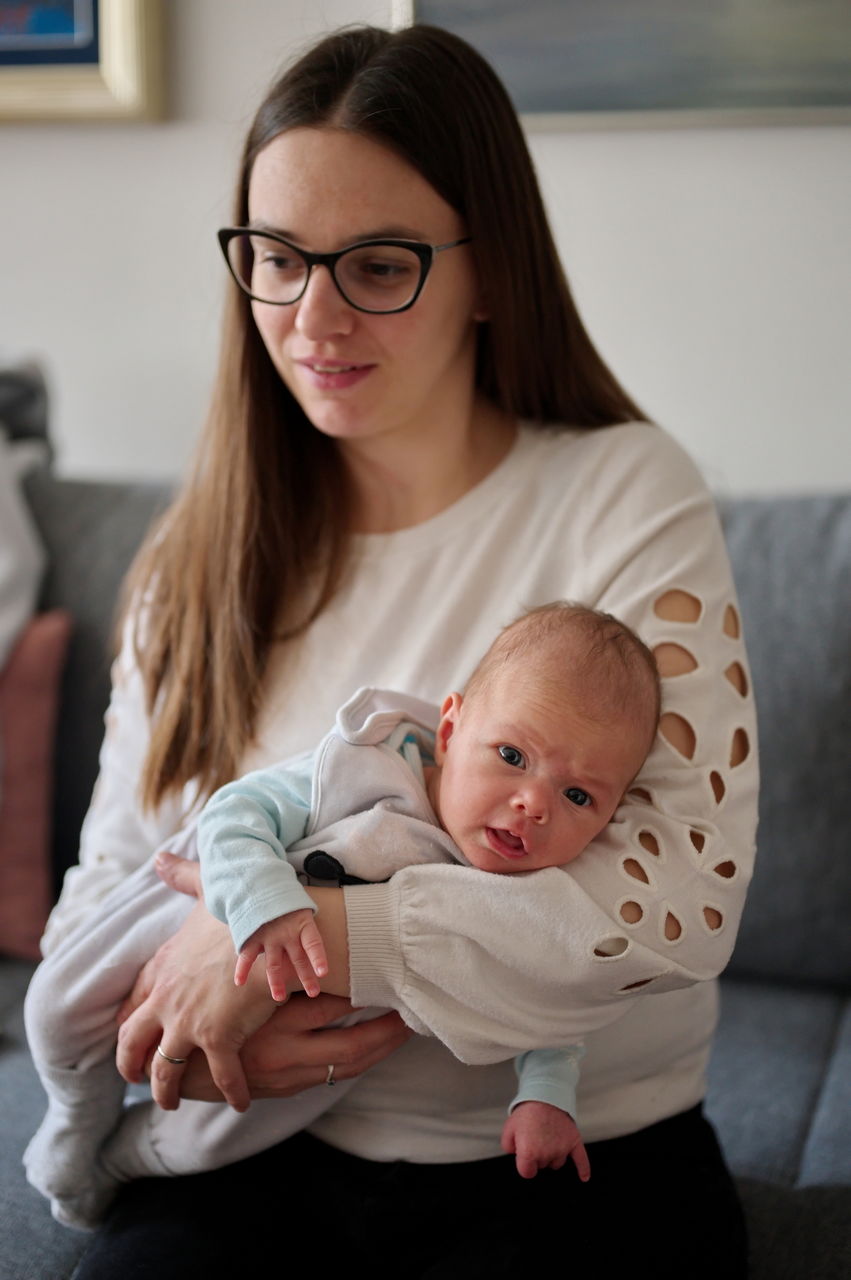 Portrait of mother sitting on a sofa and holding newborn baby