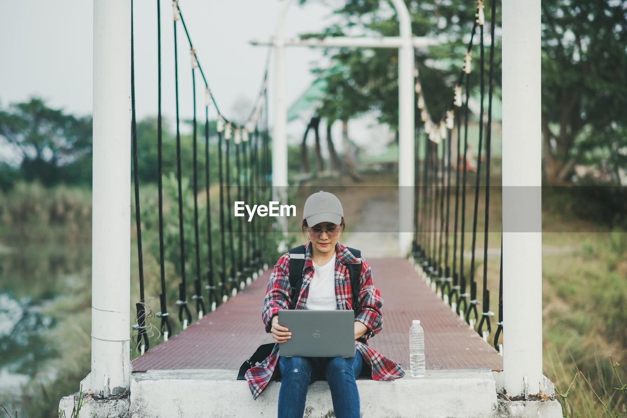 Full length of young woman standing in park using laptop