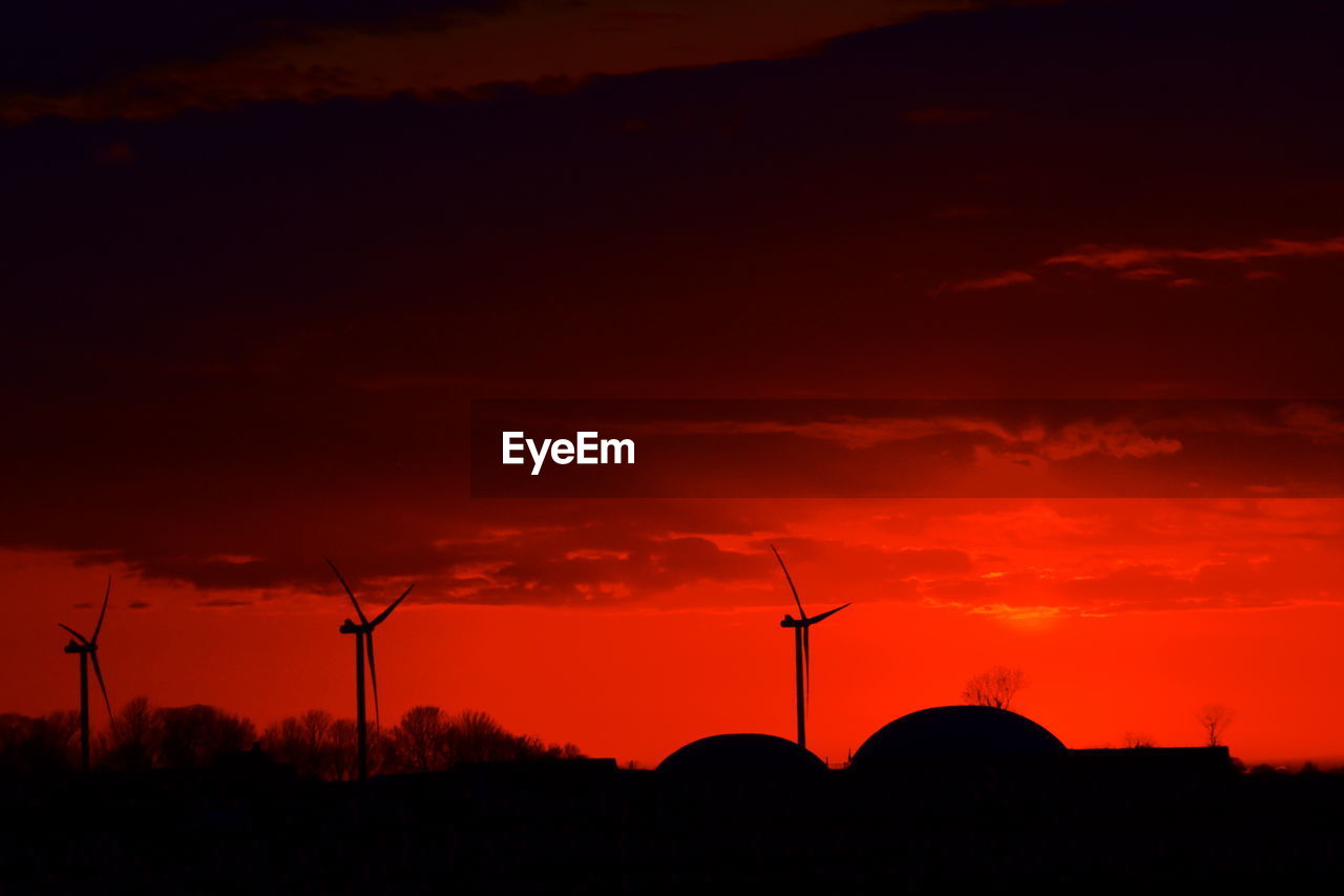 SILHOUETTE WIND TURBINES ON LANDSCAPE AGAINST ORANGE SKY