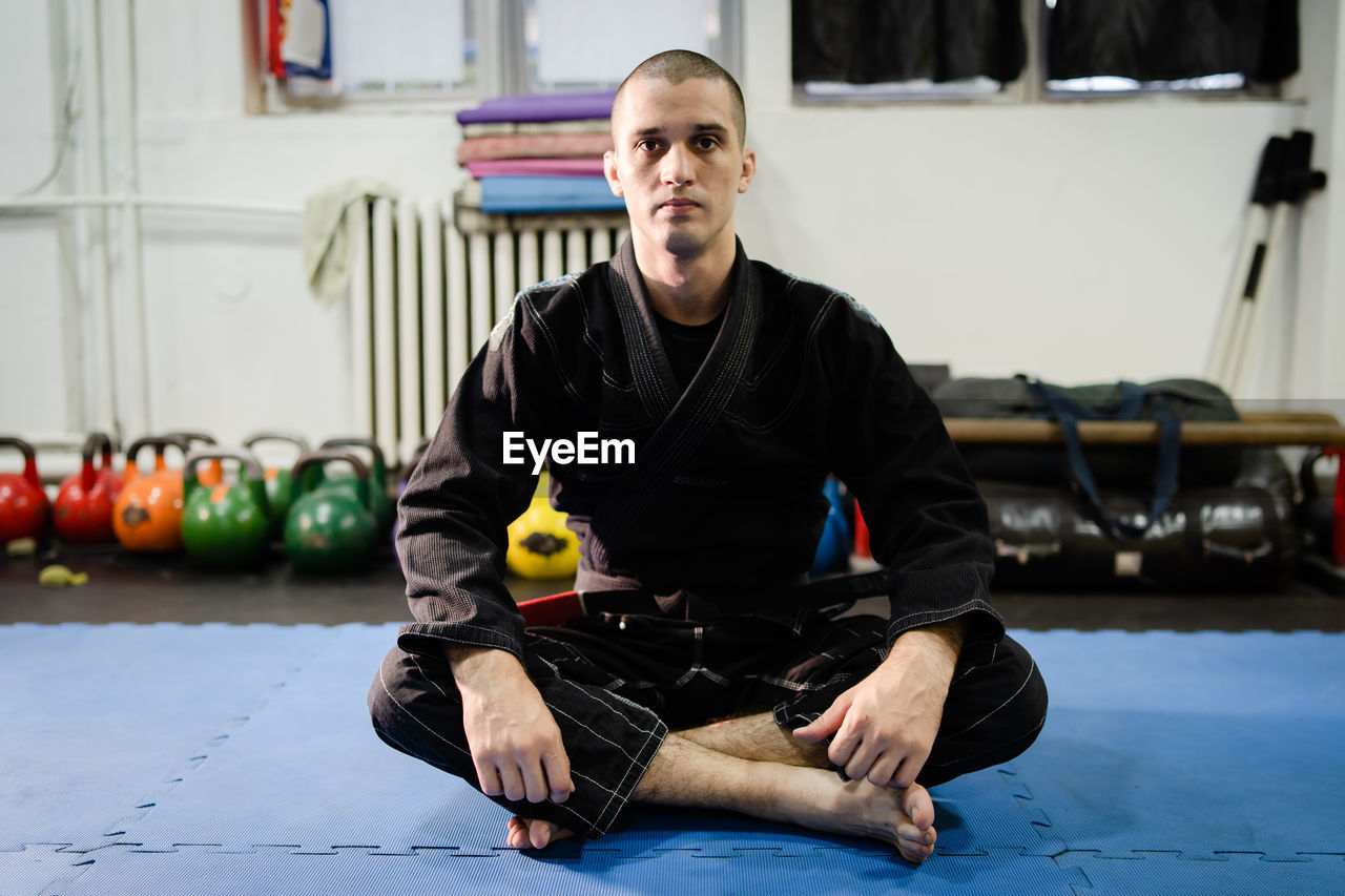 PORTRAIT OF YOUNG MAN SITTING ON FLOOR IN KITCHEN