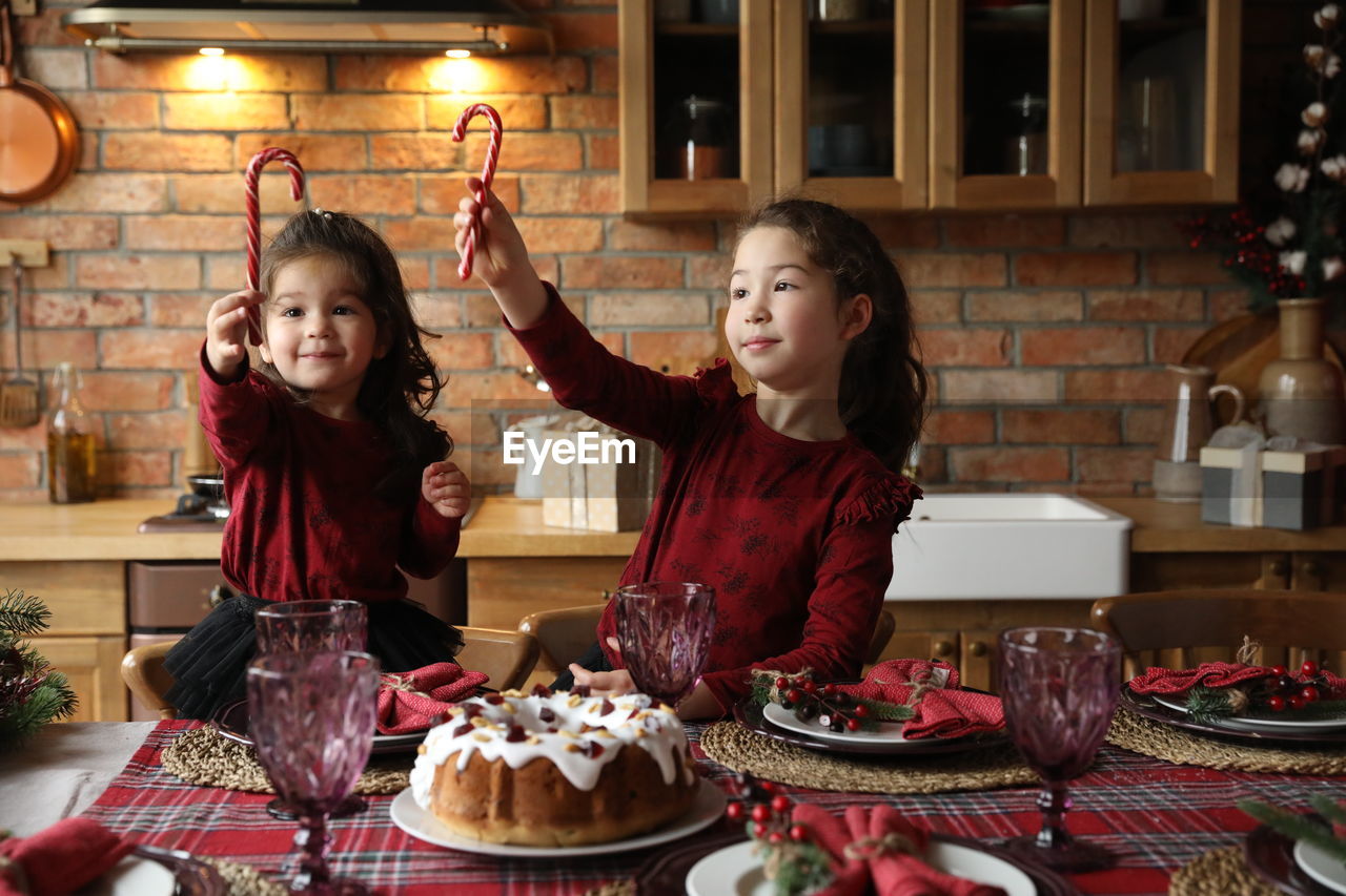 Two happy girls holding sweet at table in a christmas kitchen. 