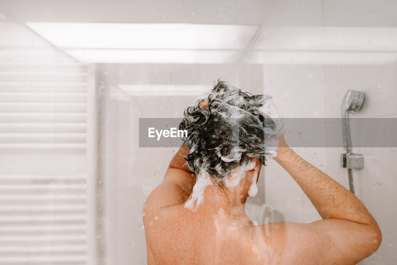 Midsection of man taking a shower in bathroom at home