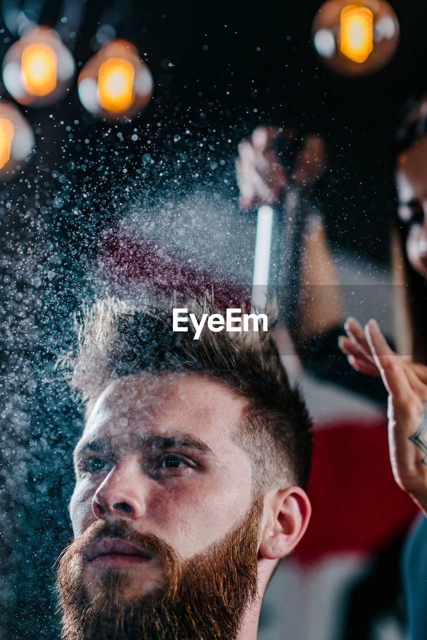 Close-up of woman spraying on man hair