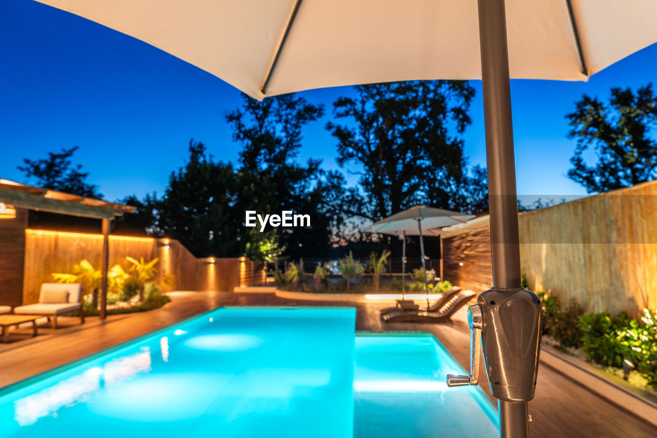 swimming pool, wealth, luxury, water, poolside, nature, tourist resort, architecture, blue, estate, patio, relaxation, tropical climate, luxury hotel, vacation, trip, tree, hotel, villa, travel destinations, tranquility, holiday, house, resort, lounge chair, night, summer, no people, building exterior, building, built structure, tranquil scene, home, chair, outdoors, elegance, illuminated, dusk, sky, plant, backyard, residential district, home ownership, holiday villa, lifestyles, hot tub, mansion, front or back yard, infinity pool, idyllic, palm tree, furniture, deck, travel, sunshade, upper class, domestic life, landscaped