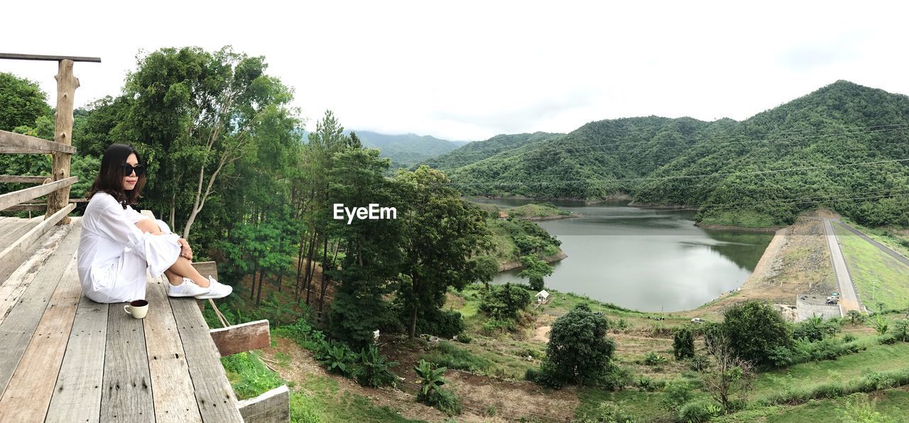 PANORAMIC SHOT OF PERSON SITTING ON LANDSCAPE AGAINST SKY