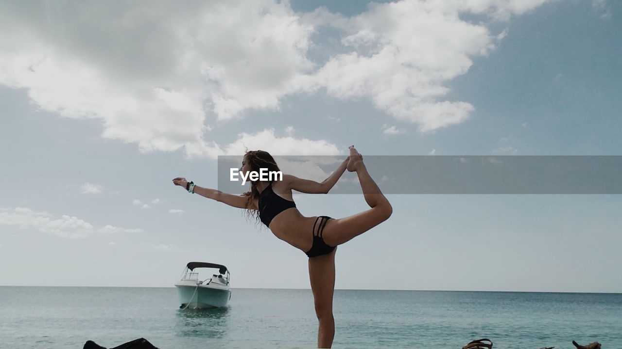 Woman exercising at beach against sky