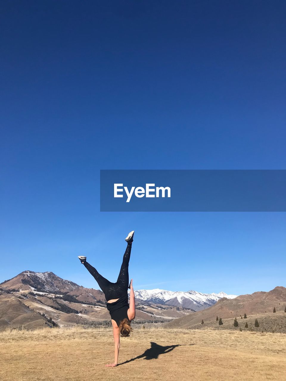 Full length of woman practicing handstand on field against clear blue sky