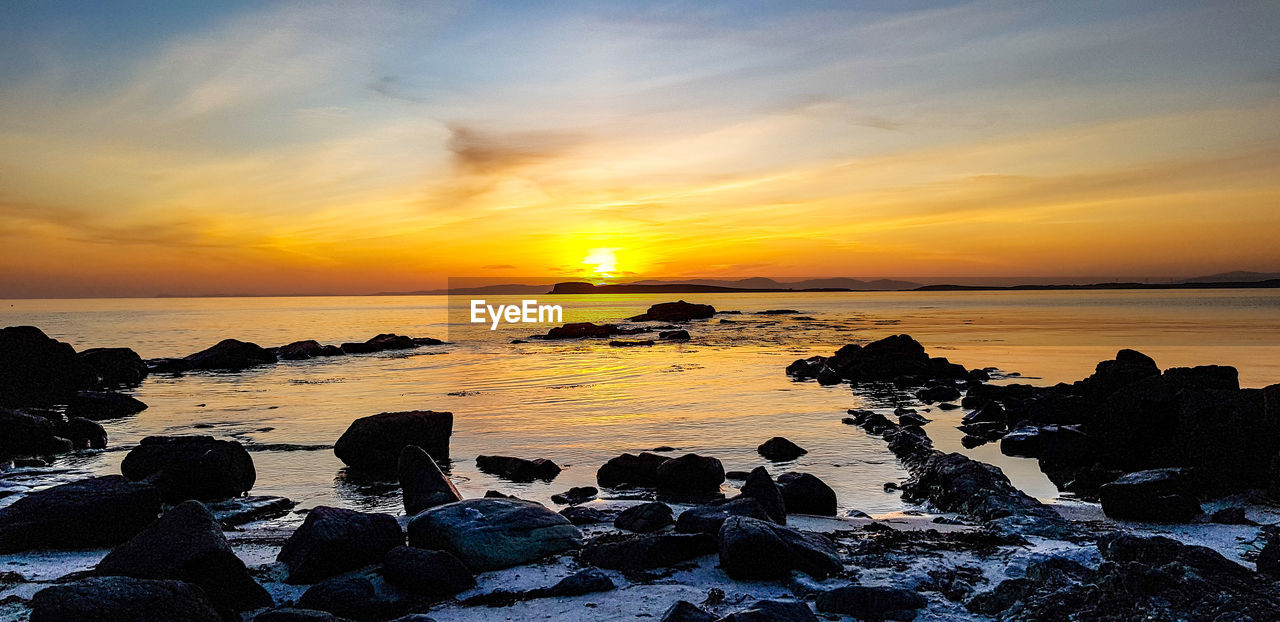 SCENIC VIEW OF ROCKS ON SEA AGAINST SKY DURING SUNSET