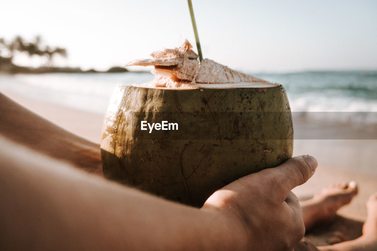 CLOSE-UP OF HAND HOLDING ICE CREAM ON BEACH