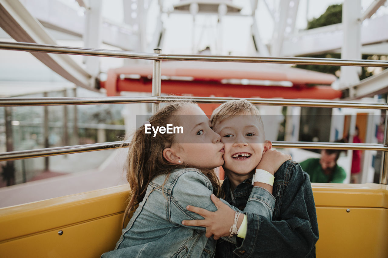 Girl kissing brother sitting in ferris wheel at amusement park