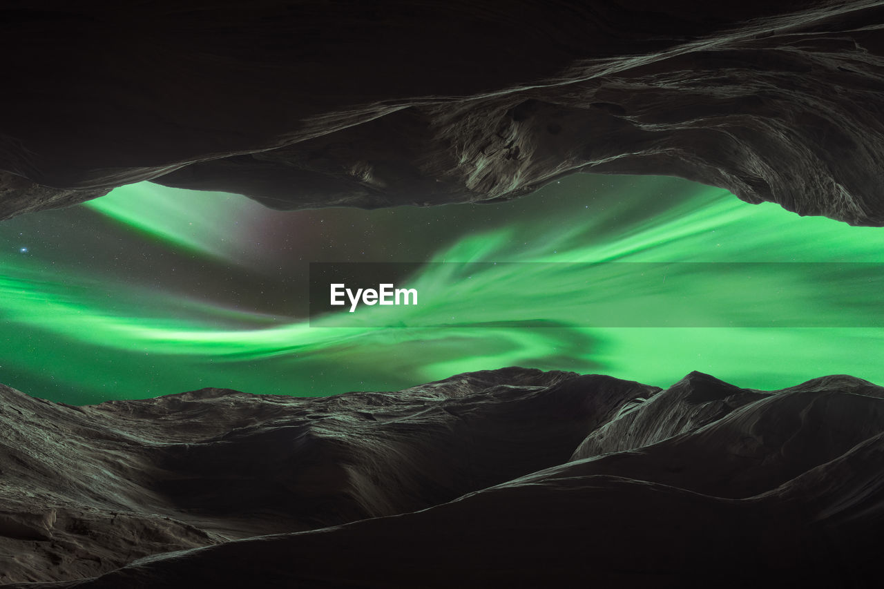 Through hole in rocky mountains view of dark night sky with glowing green polar lights in norway