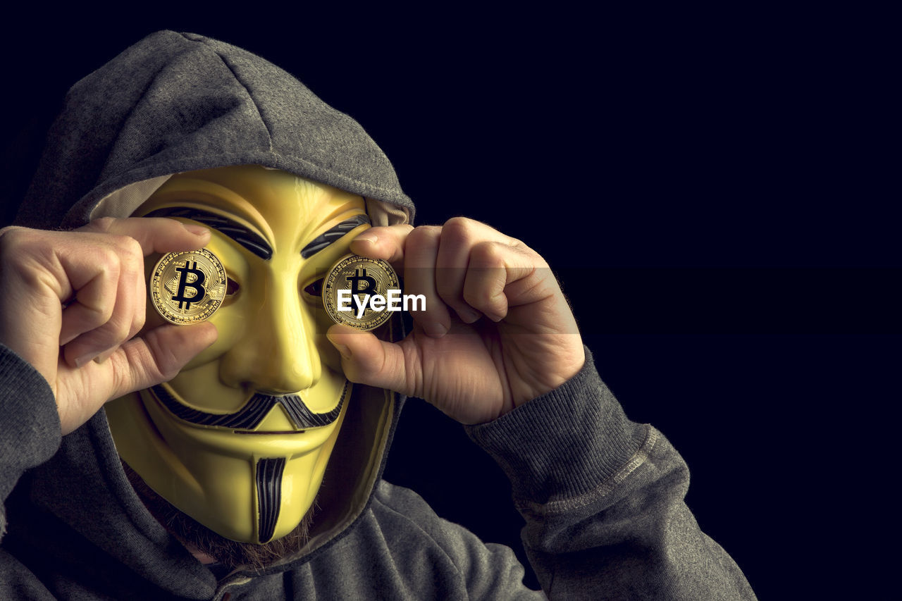 Man wearing mask holding bitcoins against black background