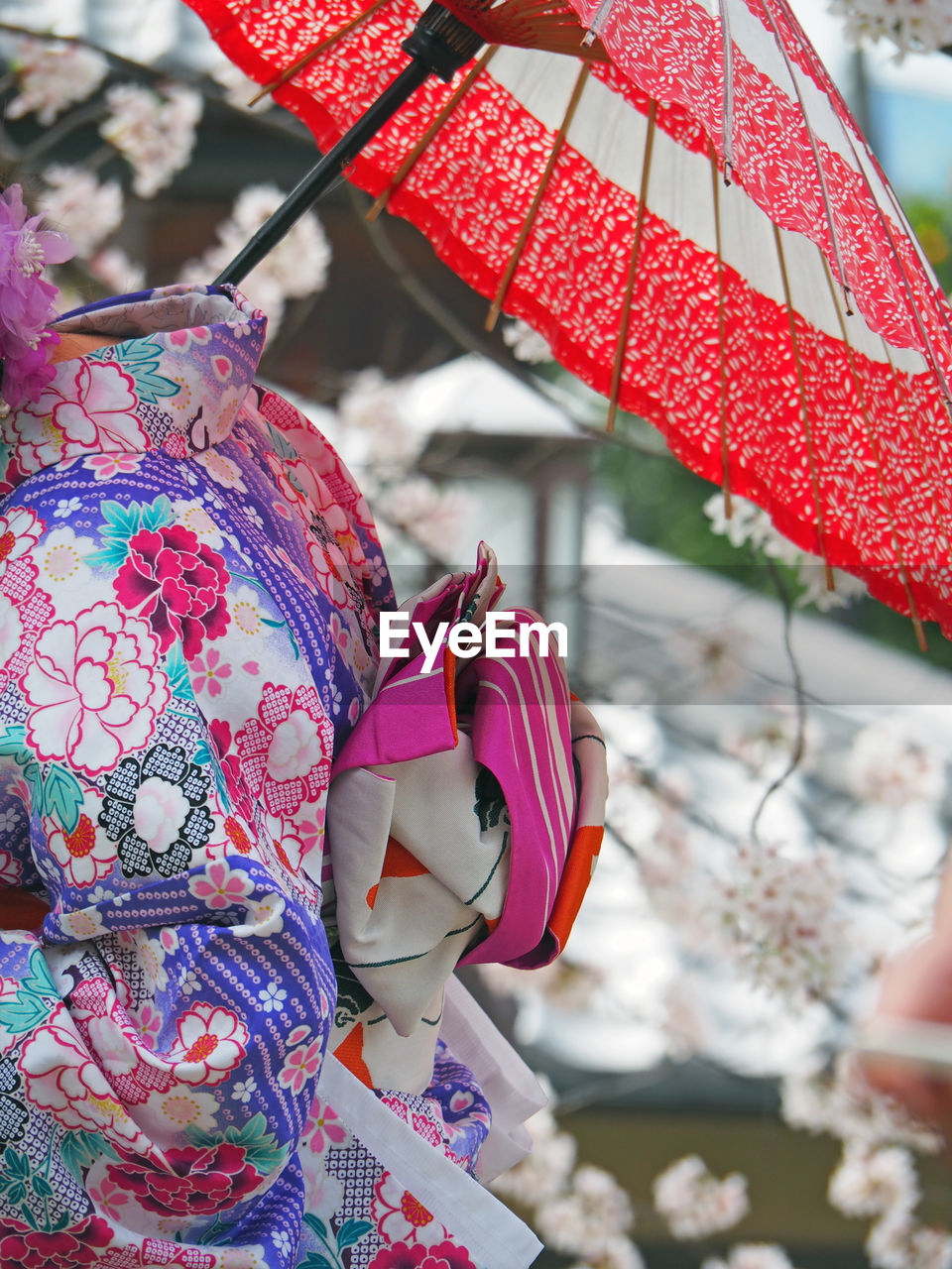 Midsection of woman wearing kimono with red umbrella against cherry tree