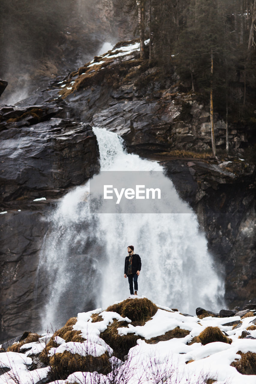 Male hiker standing on hill near waterfall in highland area in winter