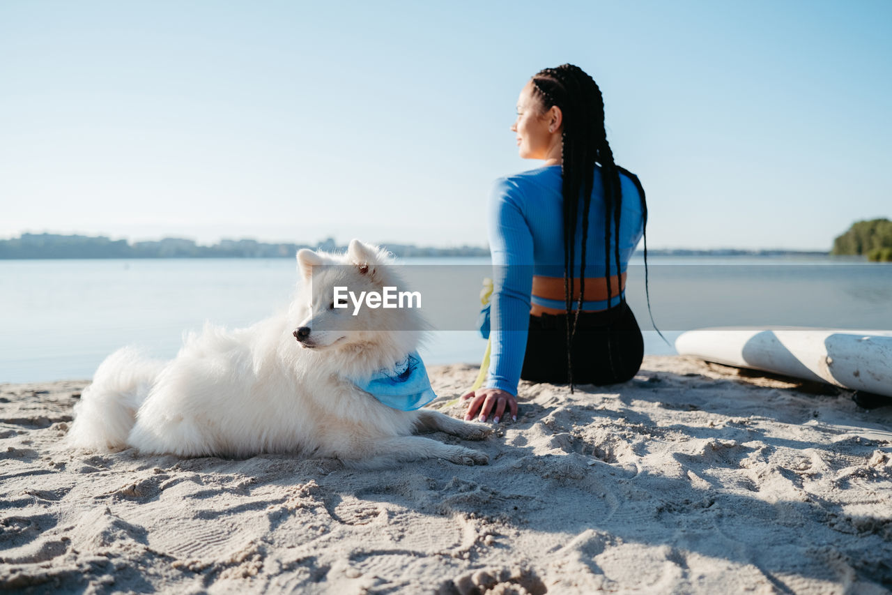 Woman with locs sitting on the beach of city lake with her best friend