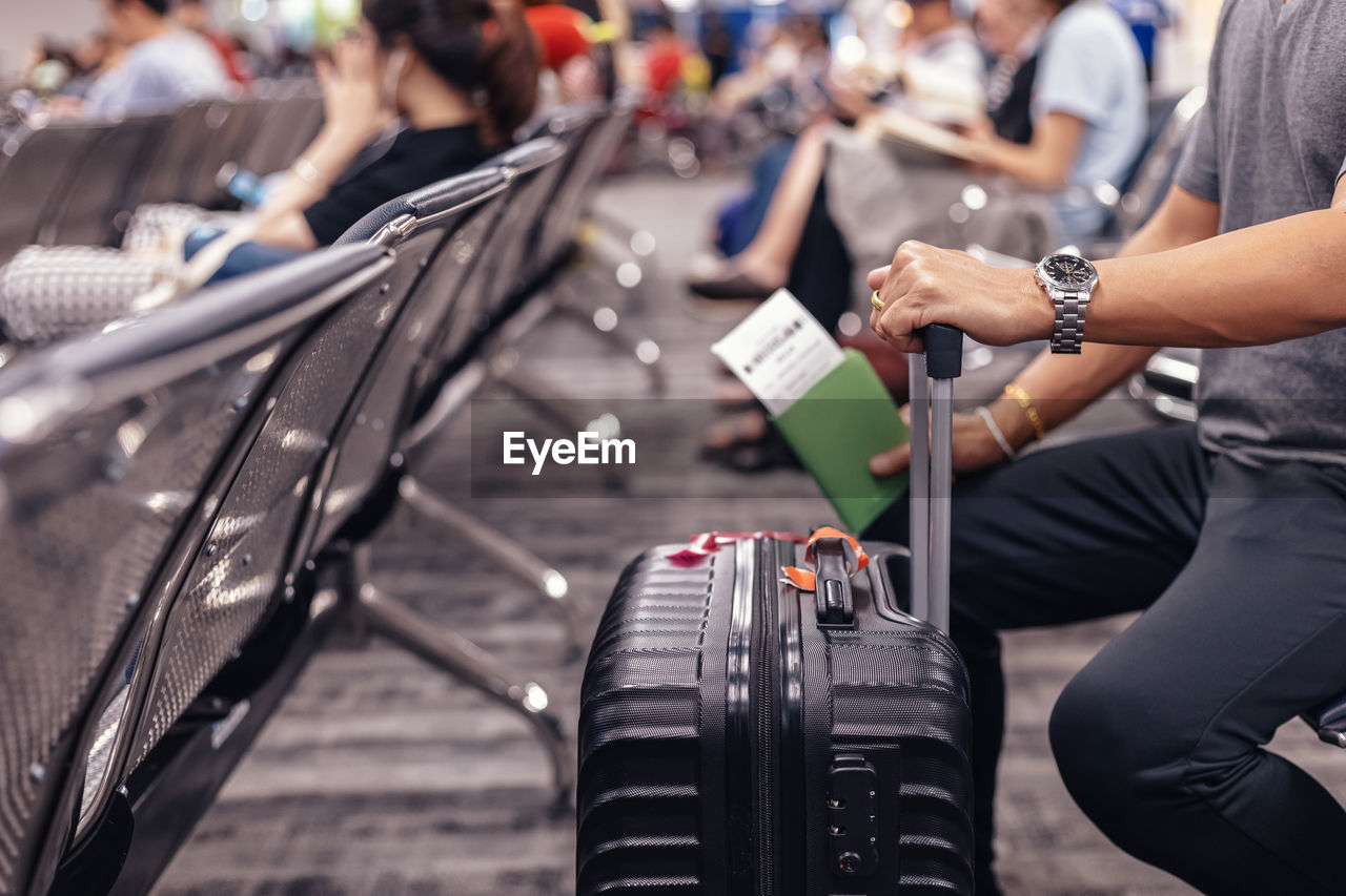 Midsection of man with luggage sitting at airport