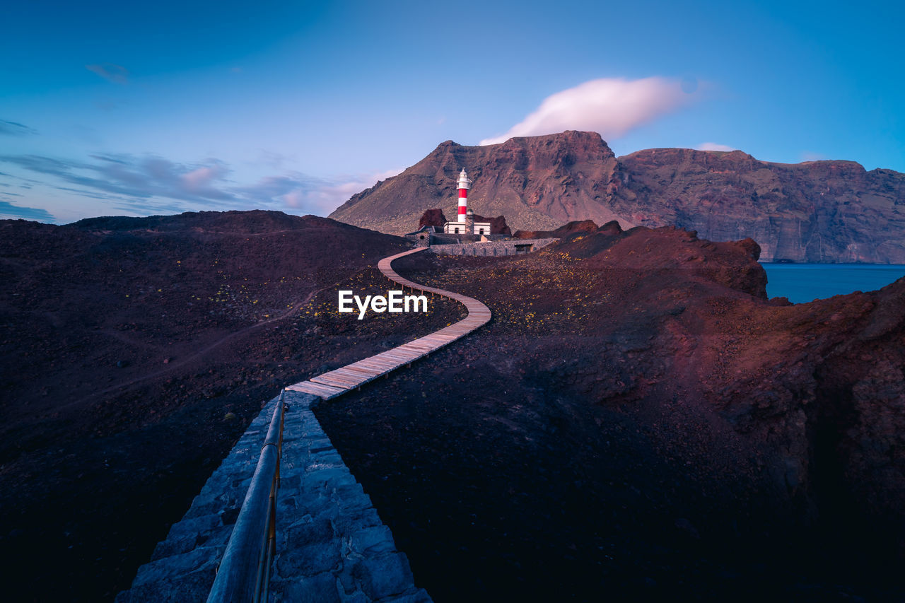 Winding pathway leading to beacon located on hill near sea on background of mountains in morning in tenerife