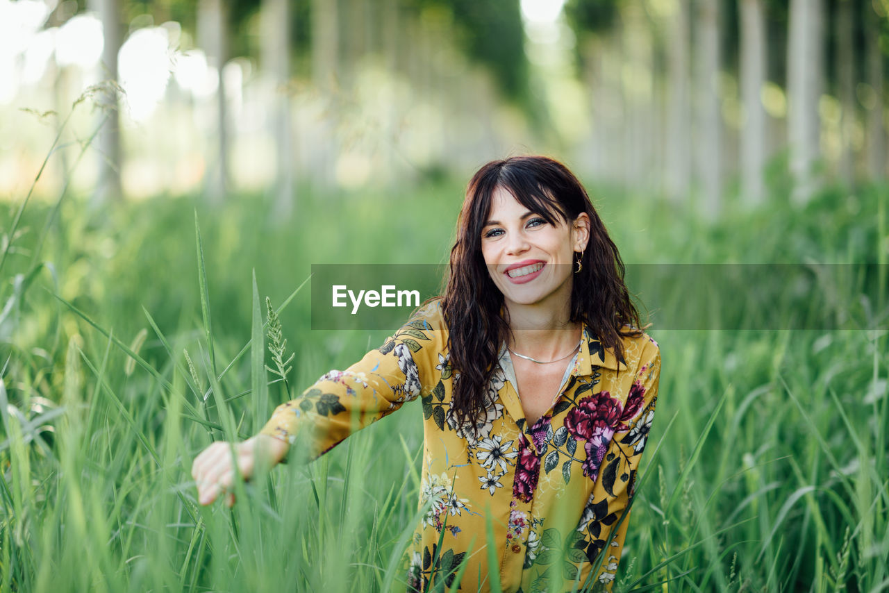 Portrait of smiling young woman standing amidst plants on field
