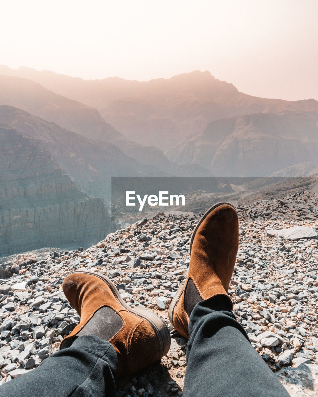 Low section of man relaxing on mountain against sky