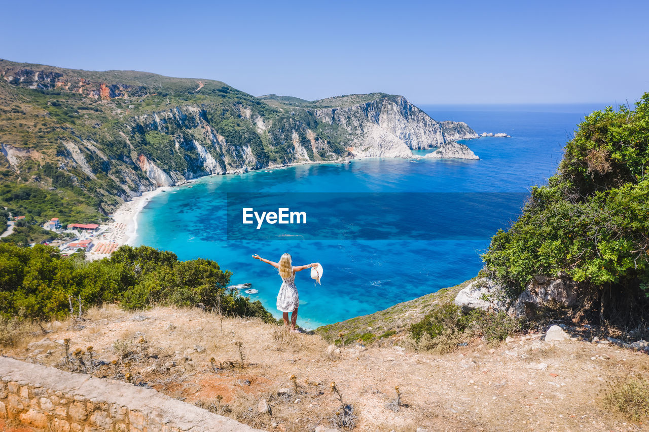 REAR VIEW OF PERSON IN SEA AGAINST SKY