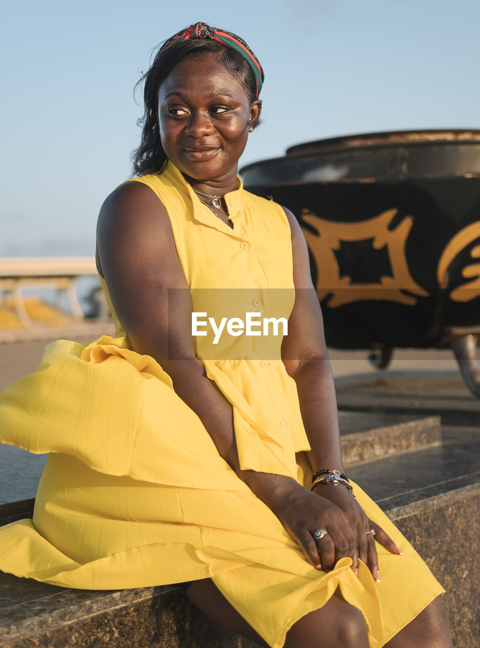 African woman sitting with yellow dress at sunset in independence arch accra ghana west africa