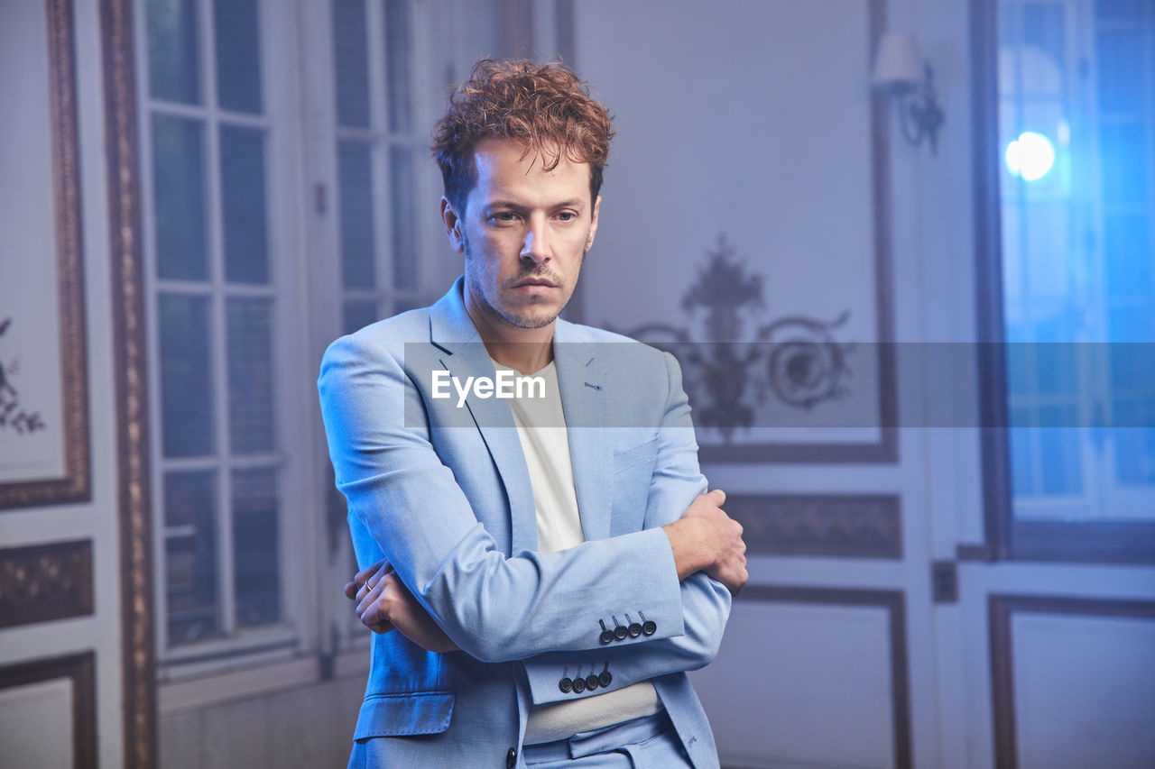 Thoughtful sad stylish male in suit sitting table in posh room and looking away